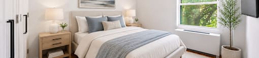 A bedroom with a large bed and a window showing greenery outside.