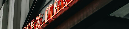 A neon sign that says "lessex market" hangs on a building.