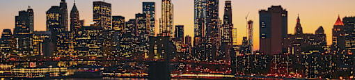 A city skyline at dusk with a boat on the water in the foreground.
