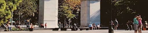 A large archway in a city square with people walking around it.