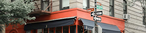 A red building with a black awning and people sitting at tables outside.