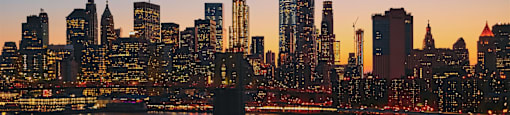 A city skyline at dusk with a boat on the water in the foreground.