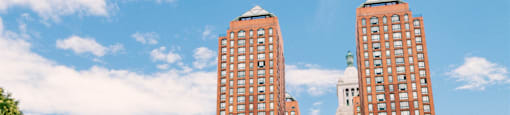 Two red brick buildings in front of a blue sky with clouds.
