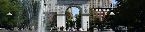A fountain in front of a large archway and buildings.