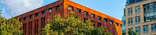 A modern building with orange panels is surrounded by trees.