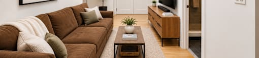 A living room with a brown couch and a painting on the wall.