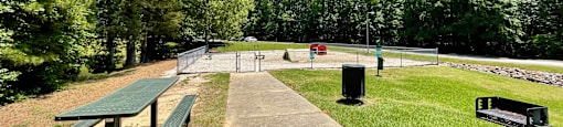 a park with a picnic table and bench and a tennis court in the background