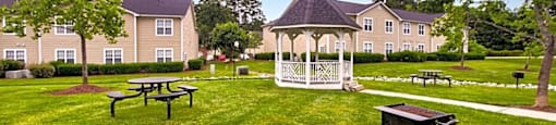 a gazebo and picnic tables in a grassy area with apartment buildings in the