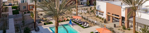 A swimming pool surrounded by palm trees and sun loungers in front of apartment buildings.