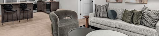 A modern kitchen with a bar stool and a grey couch with pillows.