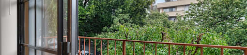 A balcony with a metal railing and a view of a green tree and a building.