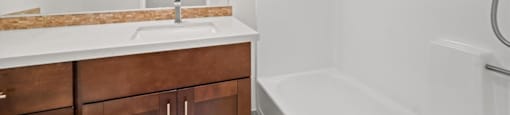 A white bathroom with a brown vanity and a white bathtub.