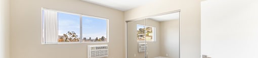 Carpeted bedroom with mirrored closet doors and window at Joro Properties Apartments, California