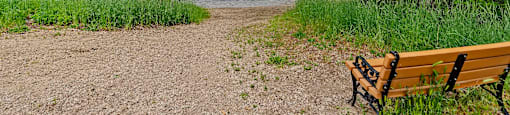 A wooden bench sits on a dirt path next to a river.