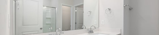 a white bathroom with two sinks and a large mirror at Ashford Townes Apartments, Fuquay-Varina