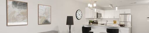 a living room with a couch and two chairs in front of a kitchen with a breakfast bar