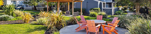 A patio with orange chairs and a table surrounded by greenery.