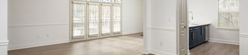 an empty living room and kitchen with wood flooring and white walls