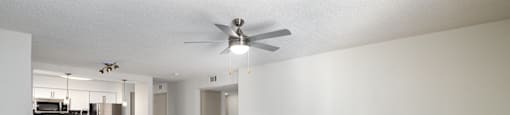 an empty living room with a ceiling fan and a kitchen