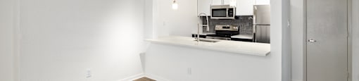 an empty living room with white walls and a kitchen