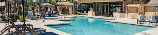 A pool area with a blue umbrella and lounge chairs.