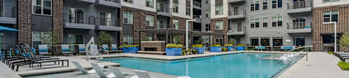 an apartment pool with chairs in front of an apartment building