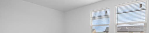 A room with a carpeted floor and two windows.