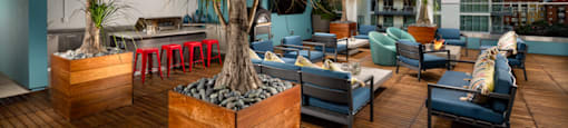an outdoor lounge area with blue chairs and blue couches on a wooden deck with palm trees at Burano, Long Beach