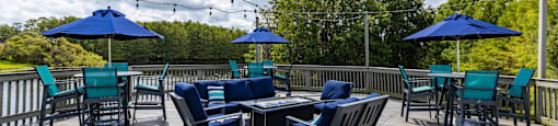 A wooden deck with blue chairs and umbrellas is surrounded by trees.