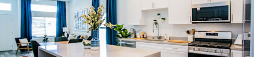 a kitchen and living room with white cabinets and a large white islandat Townes at Peace Way, Las Vegas, NV