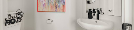 A bathroom with a white toilet, a white sink, and a colorful painting on the wall.