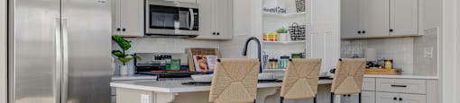 A kitchen with a refrigerator, microwave, and bar stools.