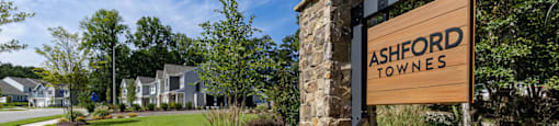 a sign for ashford towers on the side of a stone wall with a lawn at Ashford Townes Apartments, Fuquay-Varina, North Carolina
