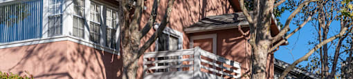 a red house with a balcony and trees in front of it