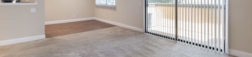 an empty living room with a large sliding glass door to a kitchen