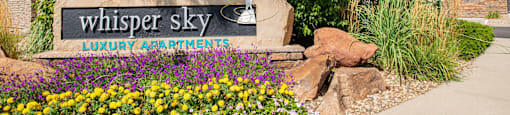 a sign for whisper sky lodges and plants in front of a building