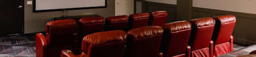 a small screening room with red leather chairs and a projector screen