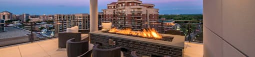A patio with a fire pit and chairs overlooking a cityscape.
