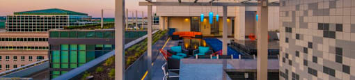 A rooftop patio with a table and chairs overlooking a cityscape at dusk.