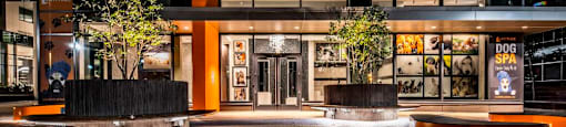 The image shows a modern building with a glass facade and a large orange pillar in front.