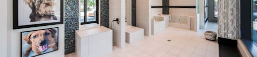 A bathroom with a white tiled floor and walls, a grey speckled wall, and a chandelier hanging from the ceiling.
