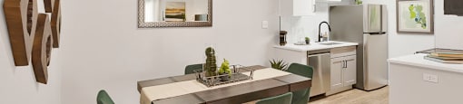 A modern dining room with a table set for two and a kitchen in the background.