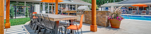 A wooden pergola with a table and chairs is in the foreground of a patio area.