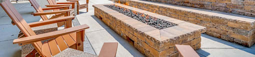 A patio with wooden chairs and a fire pit.
