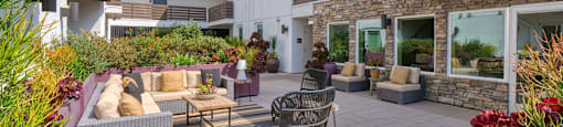 A patio with a table and chairs is surrounded by plants.