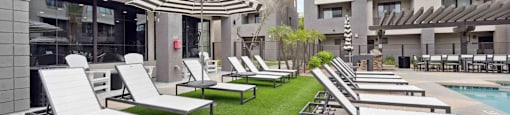 A row of sun loungers are on a lawn in front of a building.