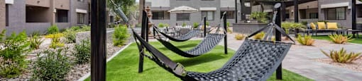 A black hammock is suspended between two poles in a grassy area.