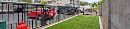 A red fire hydrant is in the foreground of a grassy area with a parking lot and buildings in the background.