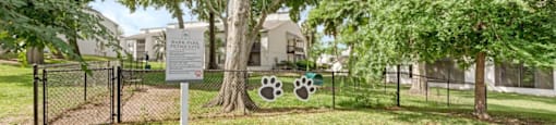 A sign with a dog paw print and bone is on a fence in front of a building.