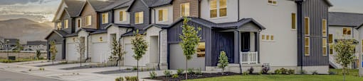 An exterior view of townhomes with front lawns, attached garages, and mountains in the background at Mt. Rainier townhouses for rent in Herriman, Utah.